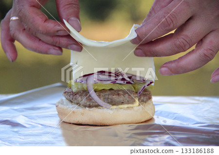 Cooking burger outdoors. Woman cooking burger. Fresh burger toppings Cooking burger outdoors. Woman cooking burger. Fresh burger toppings 133186188
