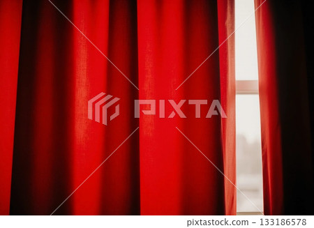 Rich red curtains frame the window, allowing soft afternoon light to filter through. The fabric adds warmth and color to the inviting interior atmosphere Generative AI 133186578