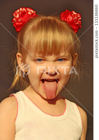 Portrait of smiling baby showing her tongue in amusing red bows 133186660