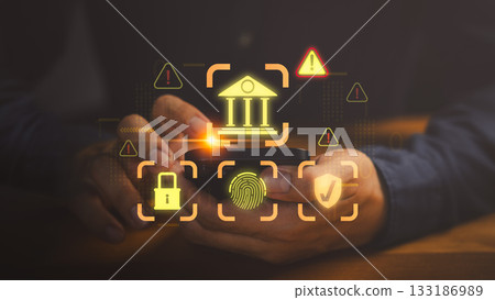 Hands holding smartphone with glowing icon of bank, fingerprint, lock, shield and warning signs, symbolizing online banking security, data protection, cybersecurity, mule account and fraud prevention. 133186989