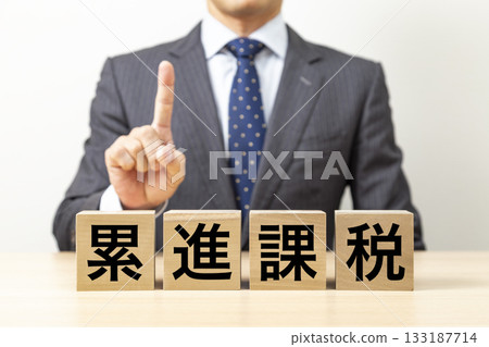 一塊寫著「累進稅」字樣的磚塊和一個商人 133187714