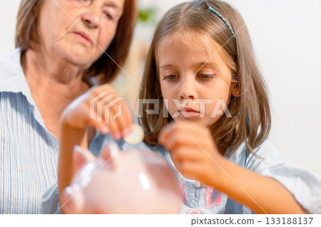 Girl saving coin in piggy bank with grandmother at 133188137
