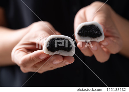 Daifuku mochi (Traditional Japanese sweet) stuffed with black sesame seed holding by hand and eating 133188282