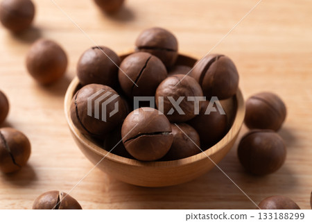Unpeeled Macadamia nuts in bowl on wooden background Unpeeled Macadamia nuts in bowl on wooden background 133188299