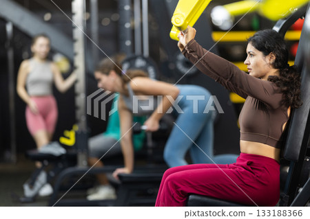 Latina woman doing shoulder press in machine 133188366