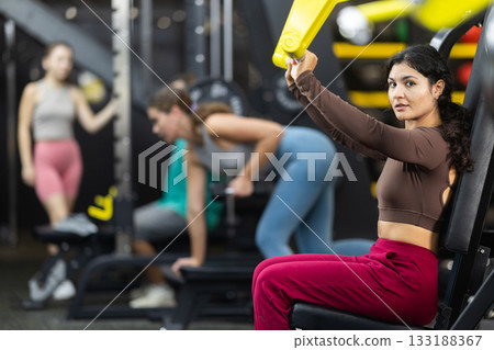 Latina woman doing shoulder press in machine 133188367