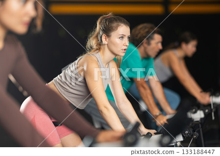 Sportive young girl doing spin bike exercises in well-equipped gym Sportive young girl doing spin bike exercises in well-equipped gym 133188447