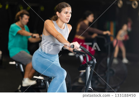 Sportive young girl doing air bike exercises in well-equipped gym 133188450