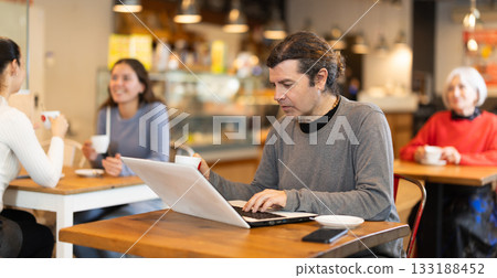 Middle aged man sitting at table, using laptop and enjoing cup of tea in coffee house. Modern lifestyle concept Middle aged man sitting at table, using laptop and enjoing cup of tea in coffee house. Modern lifestyle concept 133188452