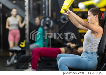 Young woman doing shoulder press while sitting in machine 133188453