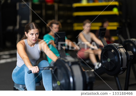 Sportive young girl training with rowing machine in sports hall Sportive young girl training with rowing machine in sports hall 133188466