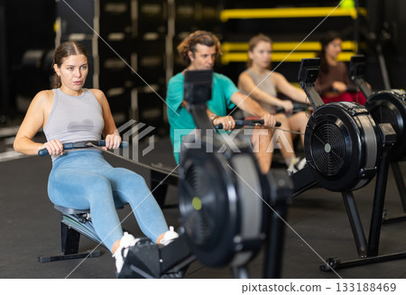 Sportive young girl training with rowing machine in sports hall Sportive young girl training with rowing machine in sports hall 133188469
