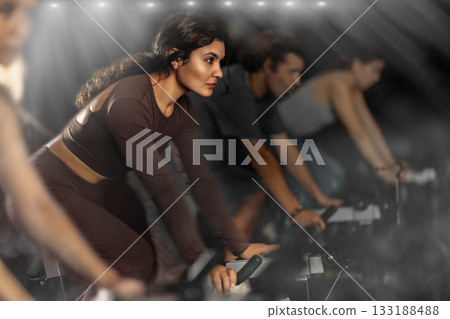 Sportive Latina girl doing spin bike exercises in well-equipped gym 133188488