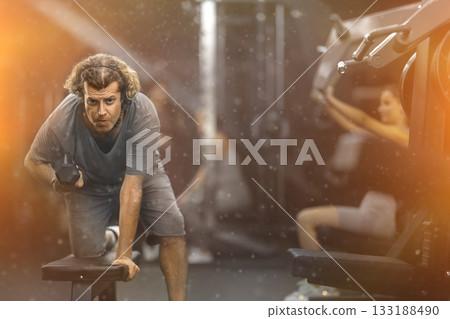 Diligent middle-aged man working out with dumbbell in sports hall Diligent middle-aged man working out with dumbbell in sports hall 133188490