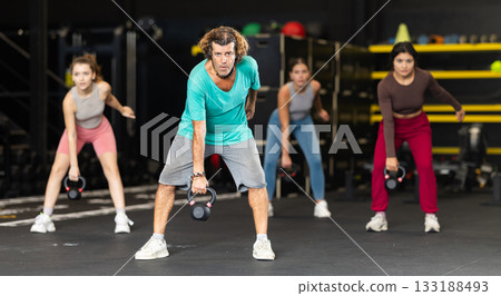 Diligent middle-aged man lifting heavy kettlebell in sports hall 133188493