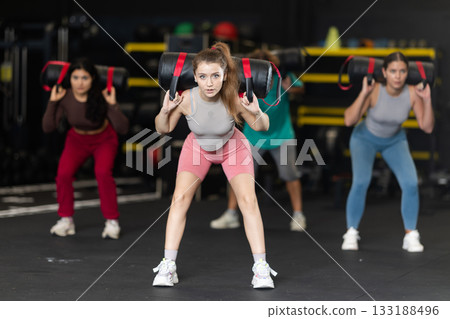 Determined young woman performing sandbag squats 133188496