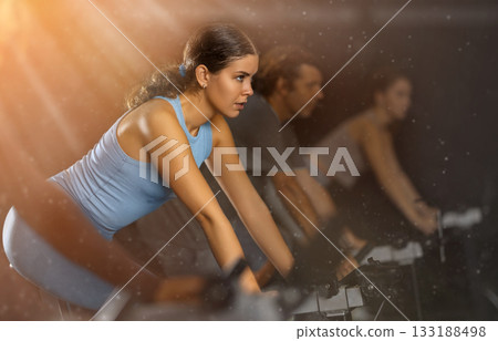 Sportive young girl doing spin bike exercises in well-equipped gym Sportive young girl doing spin bike exercises in well-equipped gym 133188498