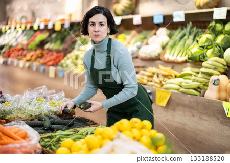 Woman shop seller puts cucumber goods on display case Woman shop seller puts cucumber goods on display case 133188520