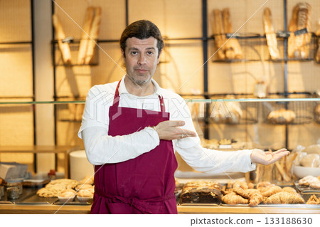Interested successful baker in maroon apron inviting to bakeshop 133188630