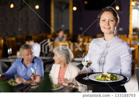 Smiling female owner of restaurant standing with serving tray Smiling female owner of restaurant standing with serving tray 133188703
