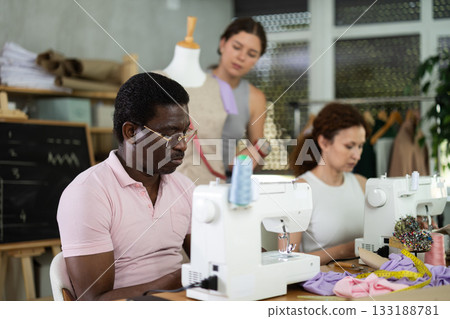 Black man working at machine during group practical sewing course 133188781