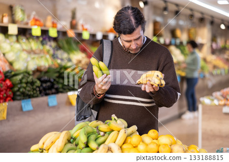 Male shopper carefully selects fresh bananas in grocery supermarket Male shopper carefully selects fresh bananas in grocery supermarket 133188815
