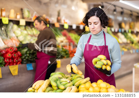 Adult woman seller puts bananas on display 133188855