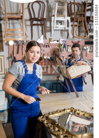 Girl restorer carefully covers carved wooden frame of antique wall mirror with thin layer of varnish Girl restorer carefully covers carved wooden frame of antique wall mirror with thin layer of varnish 133188884