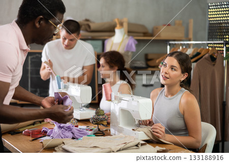 African man teacher shows student sample of pattern, another student sews and talking in background 133188916
