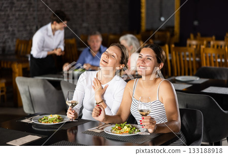 Two joyful smiling female friends having nice conversation in cafe during leisurely hearty dinner 133188918