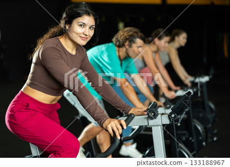 Latina woman exercising on an exercise bike in a crossfit gym Latina woman exercising on an exercise bike in a crossfit gym 133188967