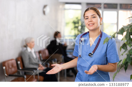 smiling female medical receptionist affably waiting for patients of clinic in waiting room 133188977
