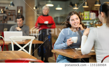 Girl in cafe sits opposite female companion, has nice conversation 133188984