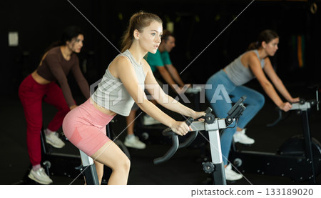 Sportive young girl doing spin bike exercises in well-equipped gym 133189020