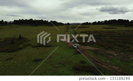 Off road vehicle driving on a dirt road in a green valley. Media Off road vehicle driving on a dirt road in a green valley. Media 133189299