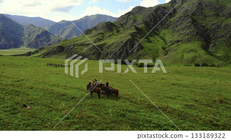 Horseback riders exploring vast green mountain valley landscape. Media 133189322