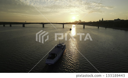 Passenger ferry navigating river at sunset near bridge and city. Clip 133189443