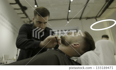 Professional barber shaving a client's beard with a straight razor. Clip Professional barber shaving a client's beard with a straight razor. Clip 133189471