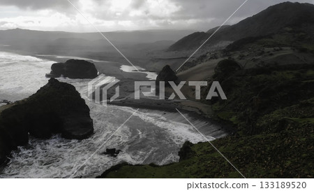 Powerful ocean waves crashing on black sand beach on cloudy day Powerful ocean waves crashing on black sand beach on cloudy day 133189520