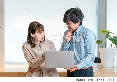 A businesswoman and a businessman with angry expressions while looking at a computer 133190091