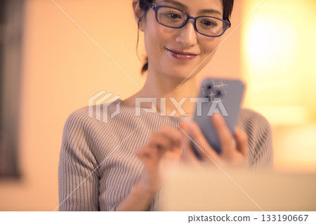 一位中年婦女在客廳一邊工作一邊看著她的智慧型手機。 133190667