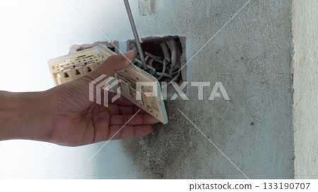 Hand of maintenance people use screwdriver unplug light switch. Socket of switch and power plug take off from outlet wall of house. 133190707