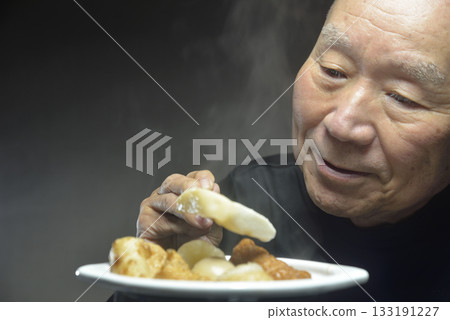 微笑的老人正在吃熱氣騰騰的關東煮。 133191227