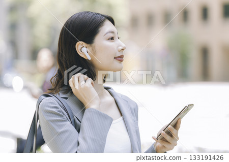 戴著耳機、手持智慧型手機的女商人的側臉照。 133191426