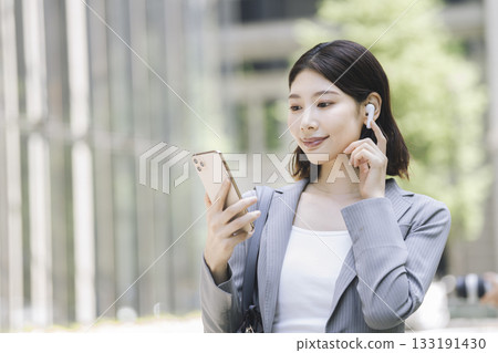 一位戴著耳機、看著智慧型手機螢幕的女商人 133191430