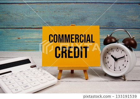 Commercial Credit text written on paper card with calculator and alarm clock on wooden background 133191539