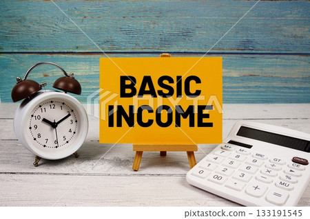 Basic Income text written on paper card with calculator and alarm clock on wooden background 133191545