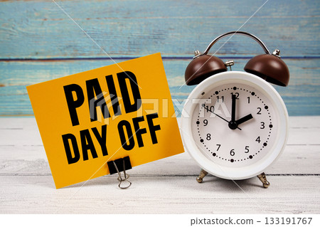 Paid Day Off text written on paper card with alarm clock on wooden background Paid Day Off text written on paper card with alarm clock on wooden background 133191767