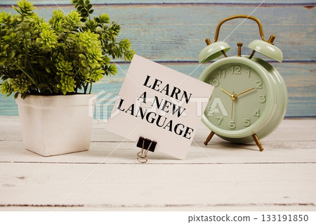 Learn a New Language text written on paper card with alarm clock on wooden background 133191850