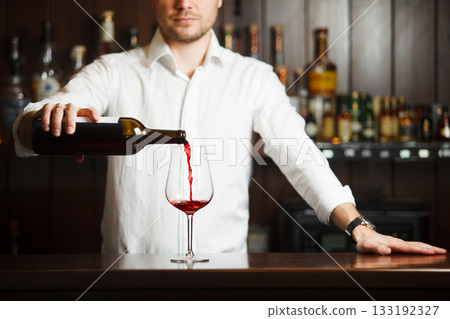 Male sommelier pouring red wine into long-stemmed wineglasses. 133192327